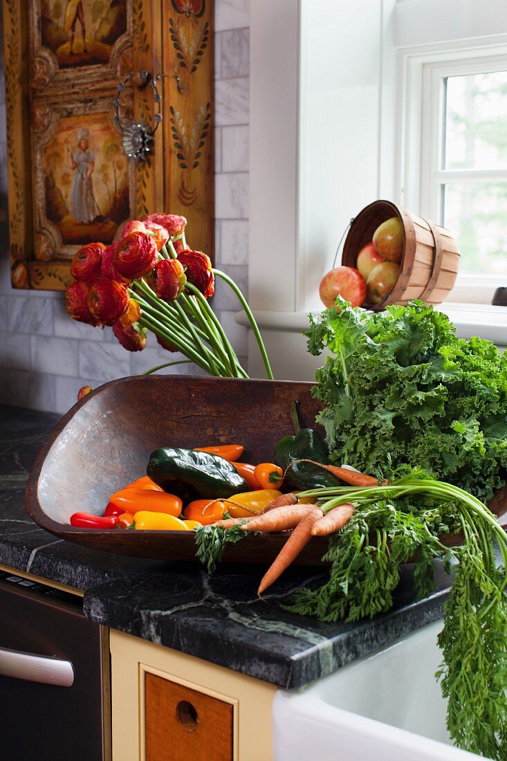 Fresh vegetables in a wooden bowl on a counter in a farmhouse kitchen