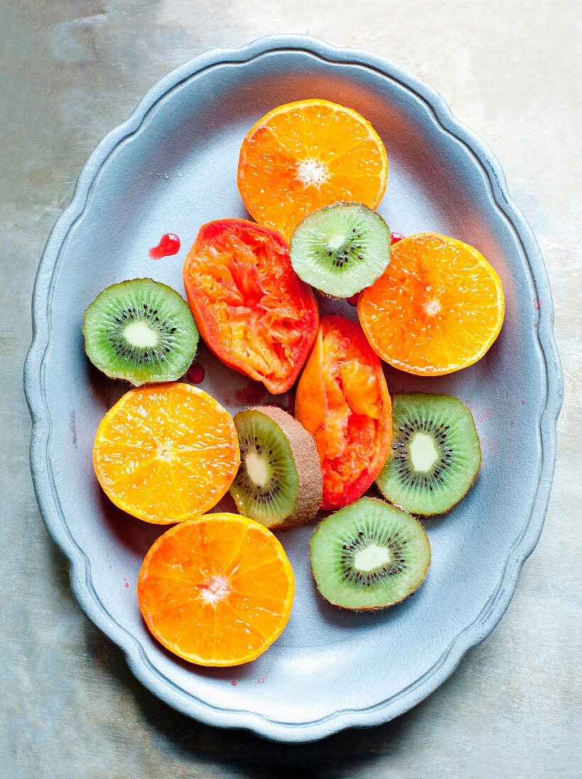 Kiwi slices, halved oranges and juiced blood oranges on a plate