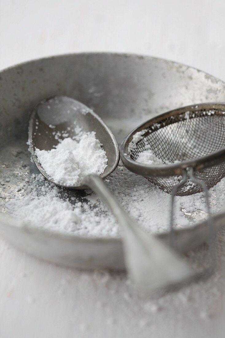 A spoon and a tea strainer with icing sugar