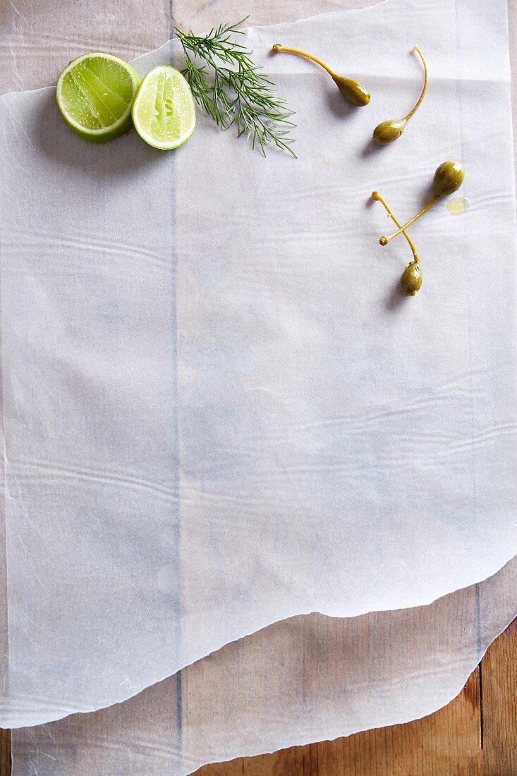 Caper fruits, a sprig of dill and limes on a piece of white paper