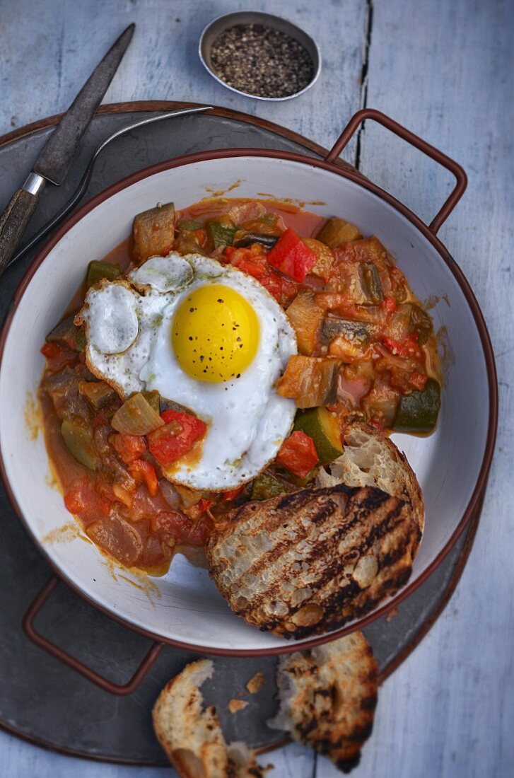 A fried egg on ratatouille with grilled bread