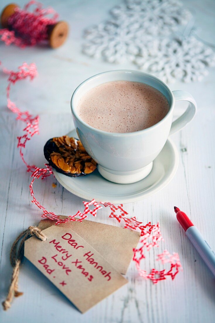 Eine Tasse heißer Kakao daneben weihnachtlicher Geschenkanhänger