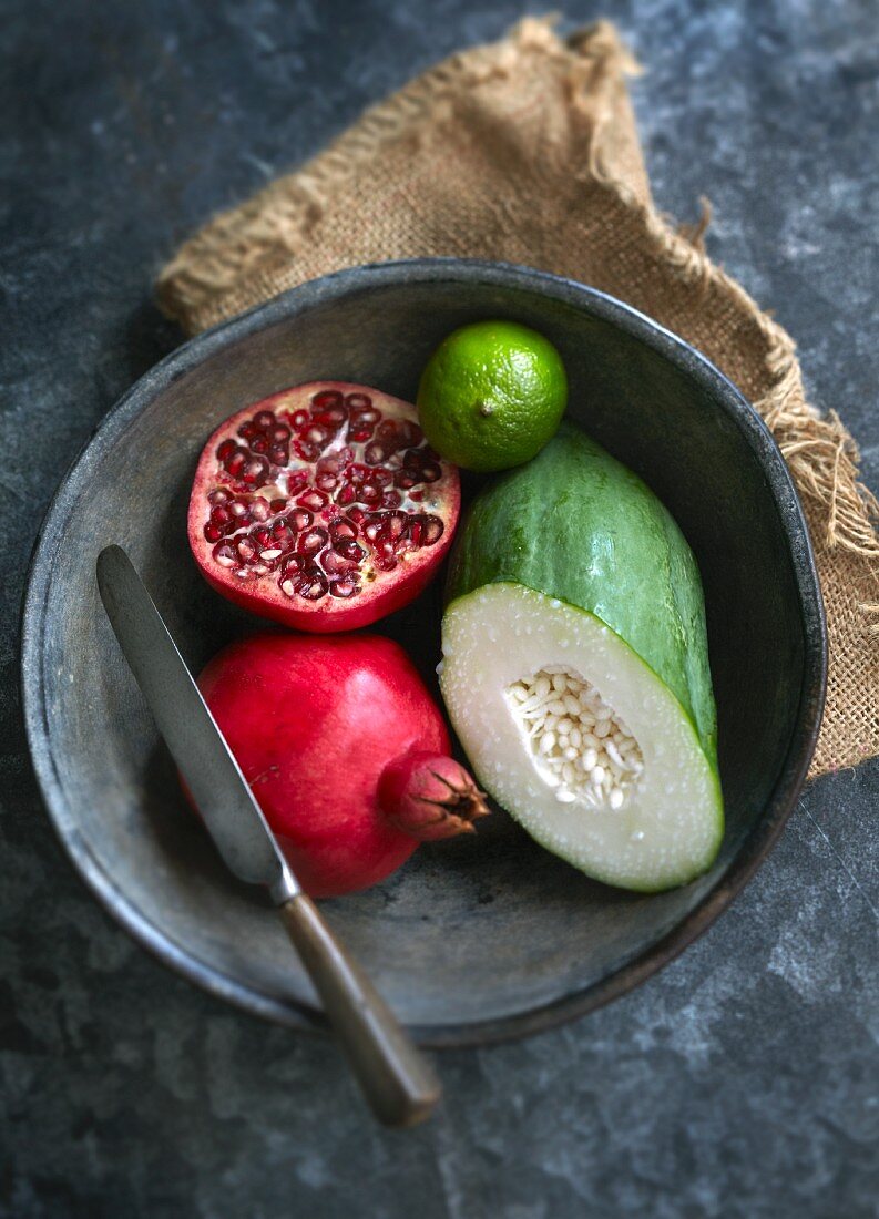 Pomegranate, vegetable papaya and a lime in a bowl with a knife