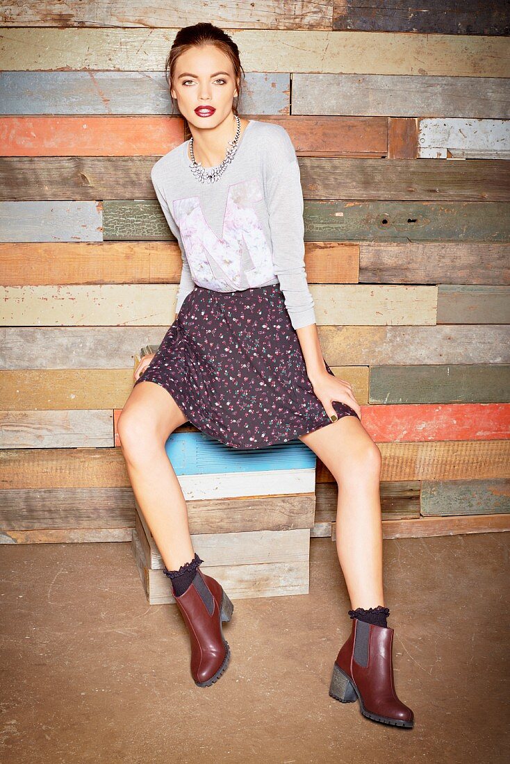 A young woman wearing a grey top, a floral patterned miniskirt and ankle boots