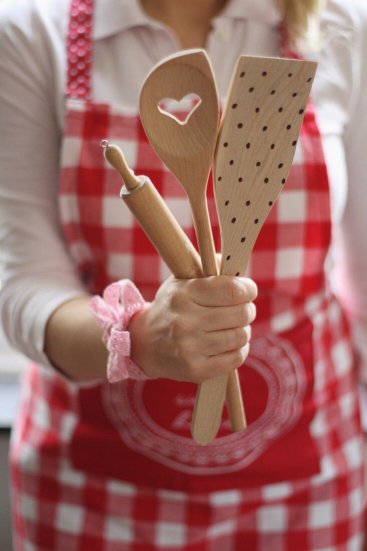 A woman wearing a red-and-white apron and a wooden spoon