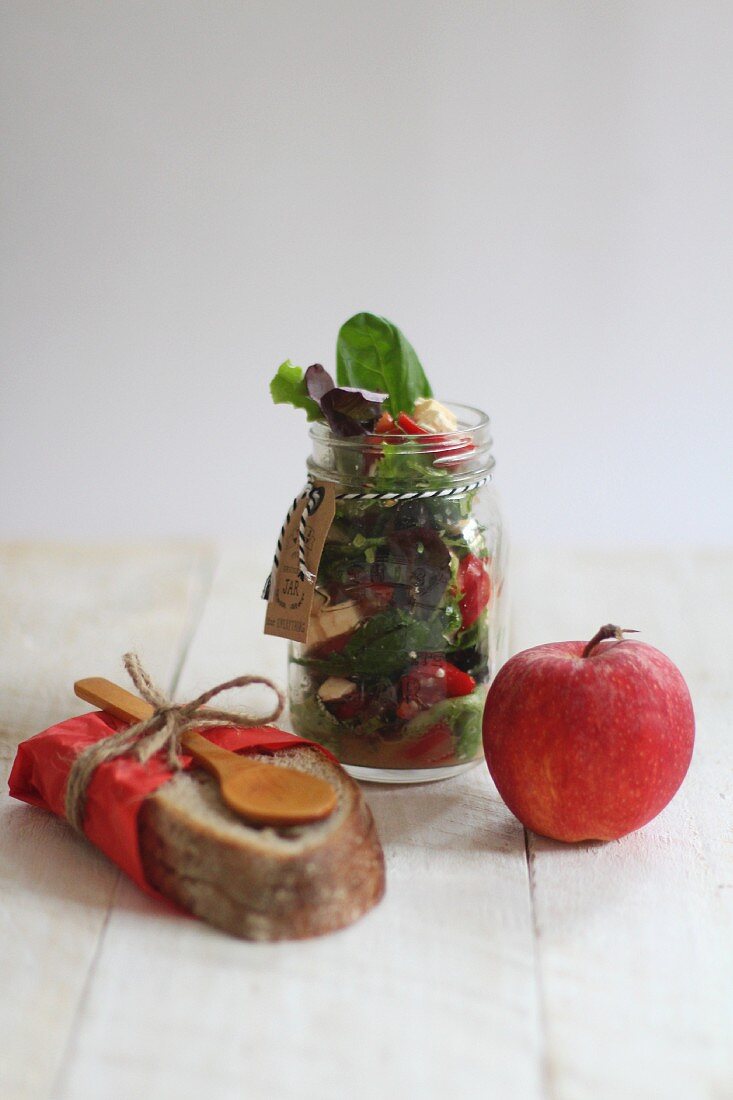 Salad in a jar with an apple and a slice of bread
