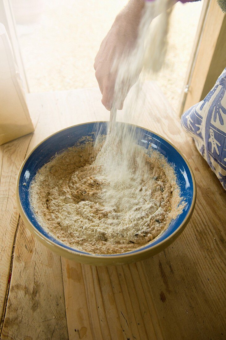 Person bereitet Brotteig zu: Mehl wird über Teig gestäubt