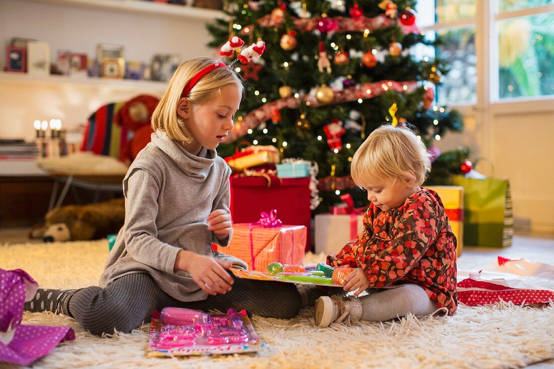 Two children unwrapping Christmas presents in front of a Christmas tree