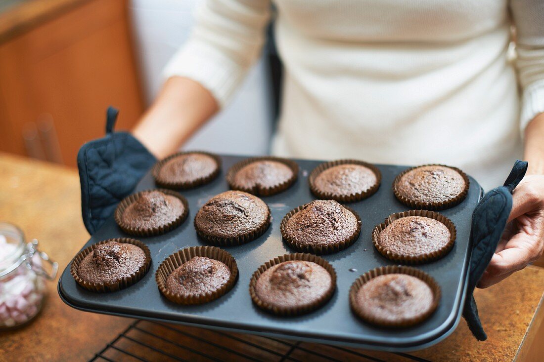 Frau hält Backblech mit frisch gebackenen Muffins in den Händen