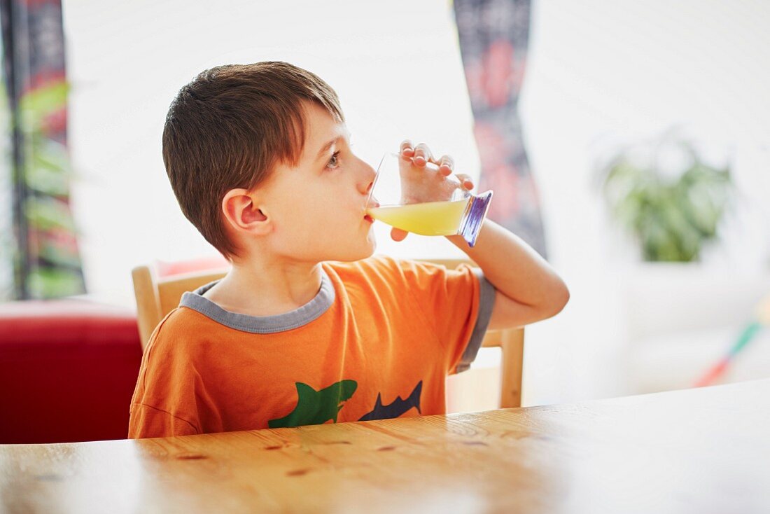 A boy sitting at a table drinking a glass of juice