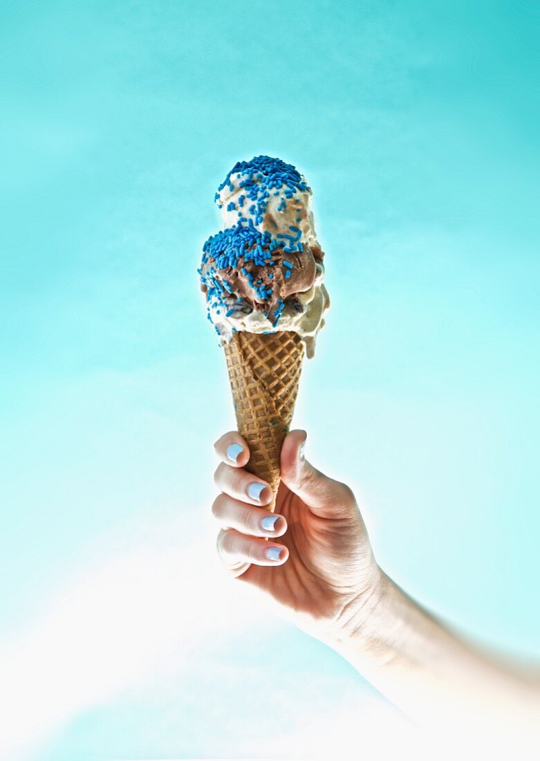 A hand holding an ice cream with blue sugar sprinkles