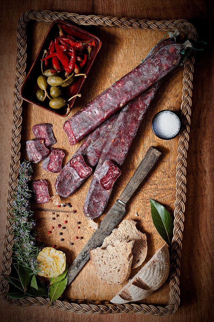 Sliced beef salami on a wooden tray with bread and salt