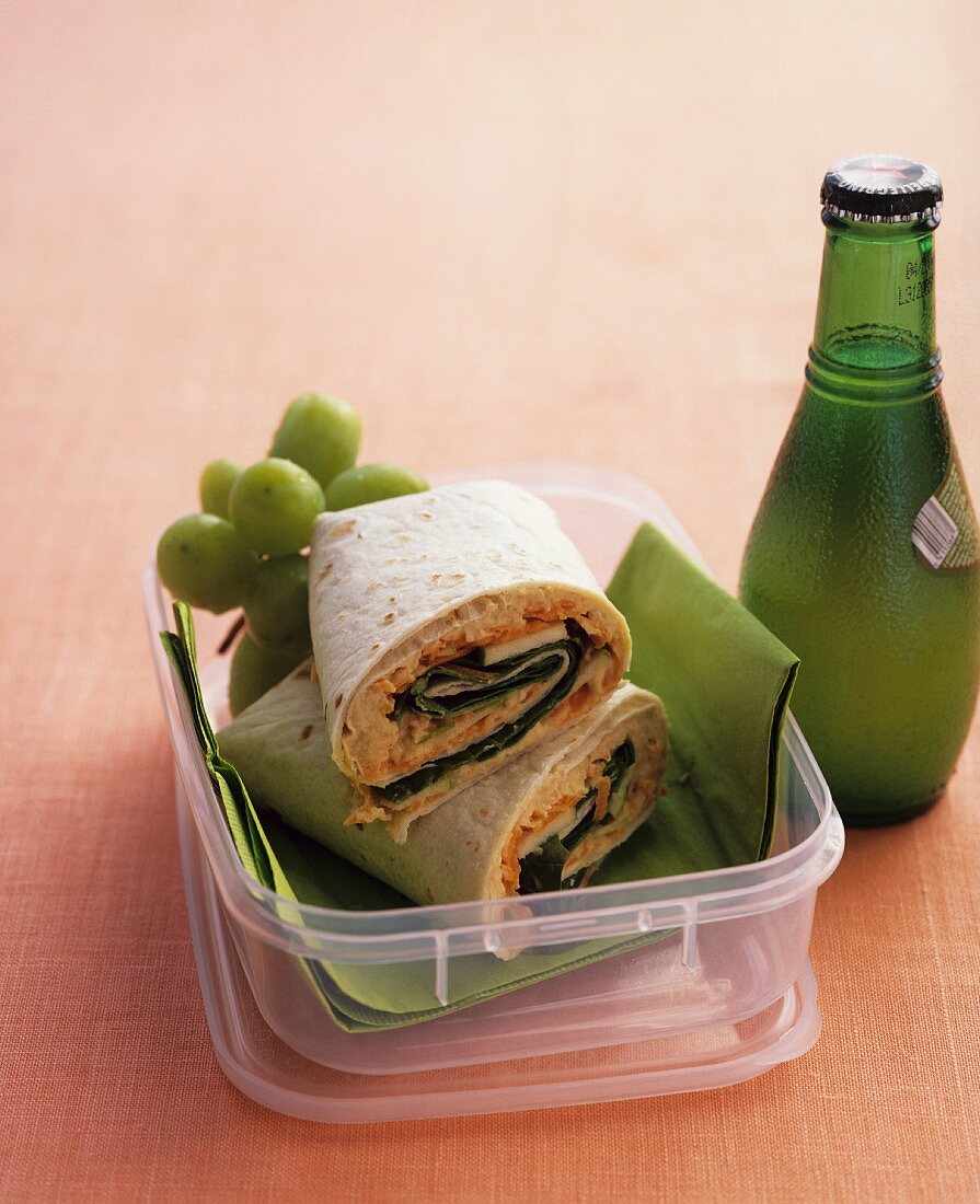 Wraps and grapes in a lunchbox with a bottle of mineral water next to it