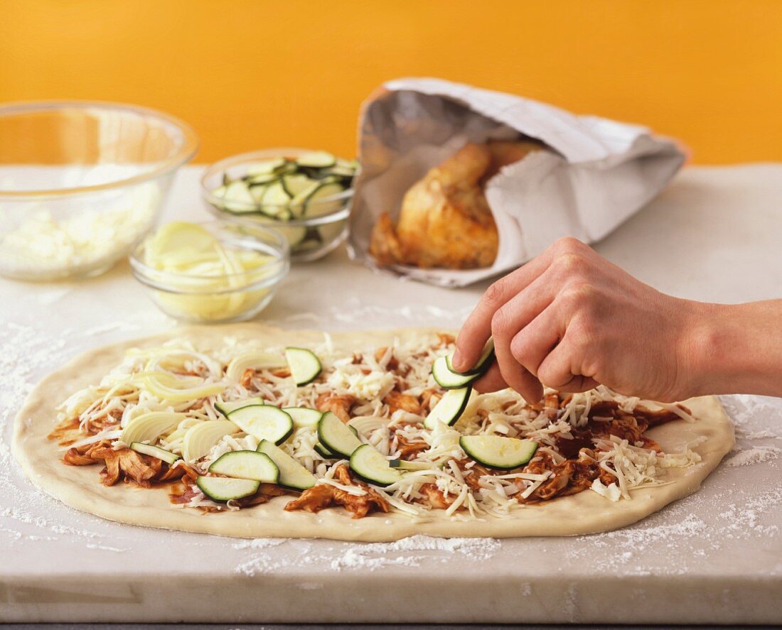 A pizza being topped with courgette slices