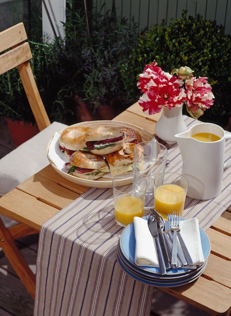 Breakfast table laid on the terrace of an inner-city apartment with bacon bagels and orange juice