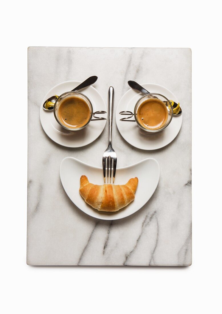 A breakfast face made from coffee cups and a croissant