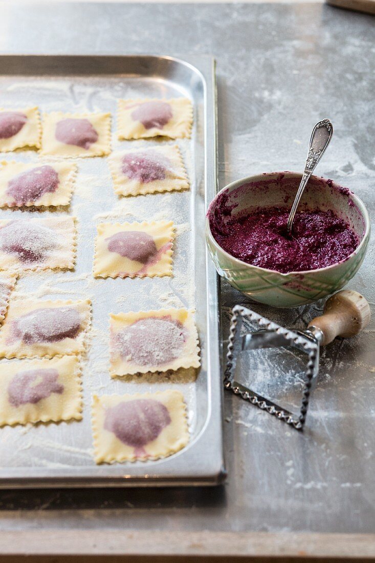 Beetroot ravioli on a baking tray with a bowl of beetroot filling and a cutter