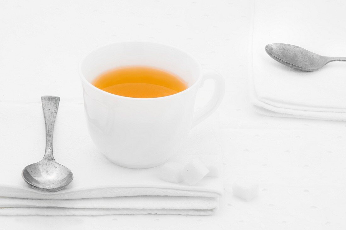 A cup of tea with sugar lumps and spoon on a white fabric napkin