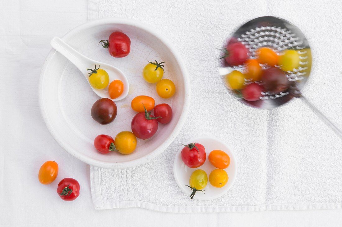 Verschiedenfarbige Tomaten in Porzellanschale & auf Sieblöffel