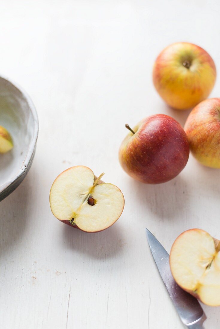Äpfel auf weißem Untergrund mit halbiertem Apfel und Messer