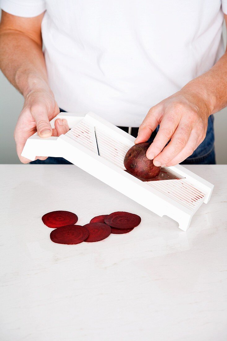 Beetroot being sliced with a vegetable slicer