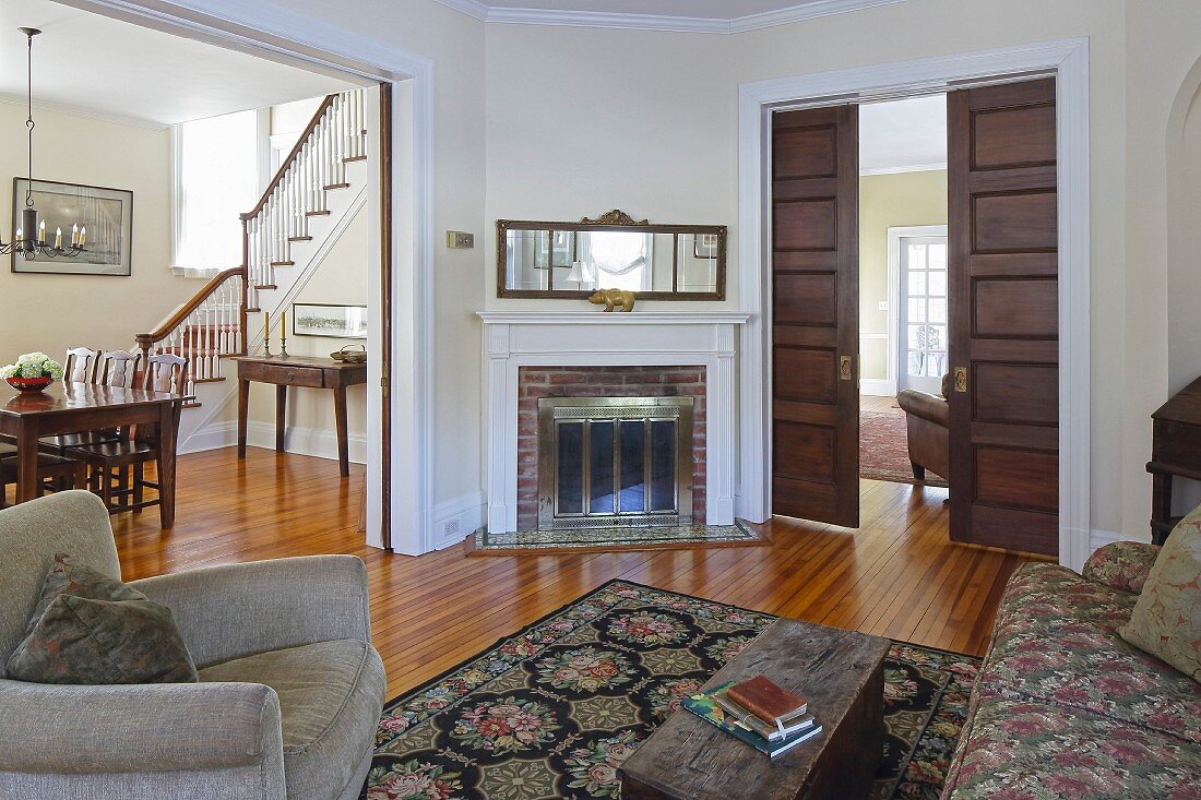 Armchair and sofa in living room with wide, open doorway with view of dining area and staircase