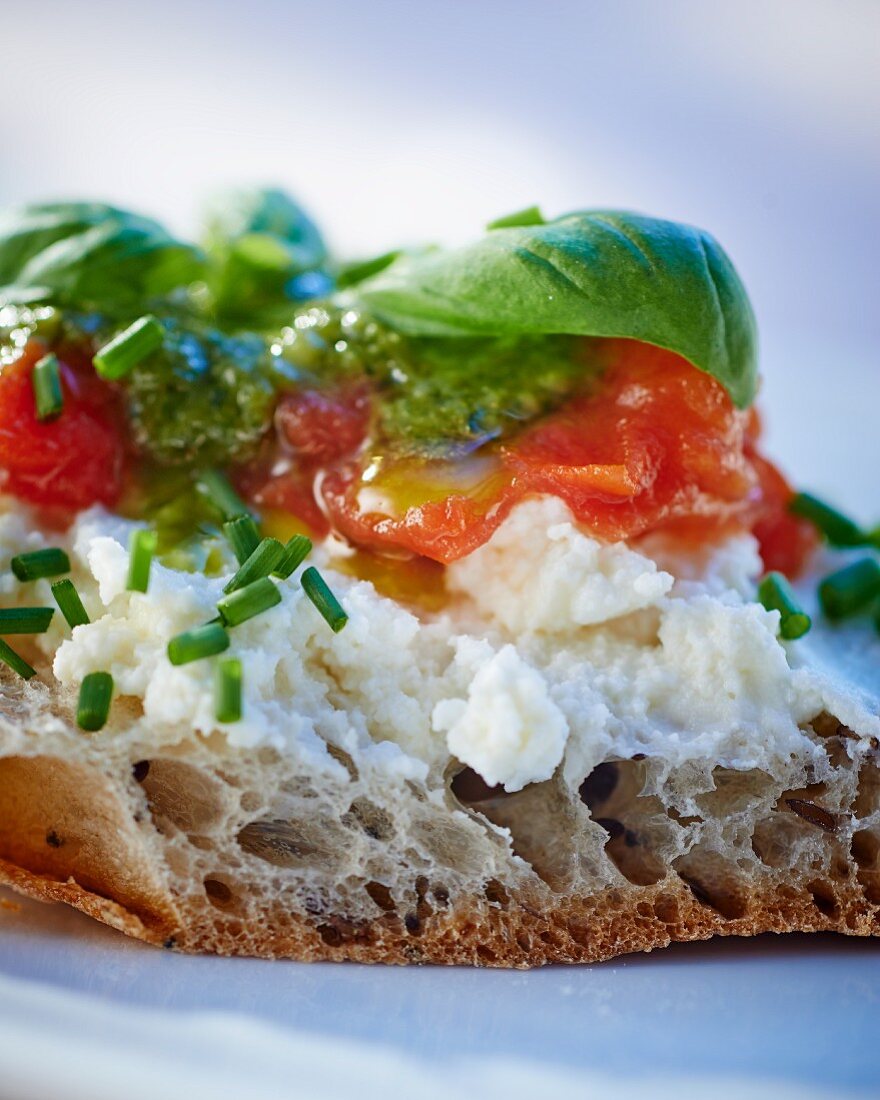 A slice of bread topped with goat's cheese, pesto and tomatoes