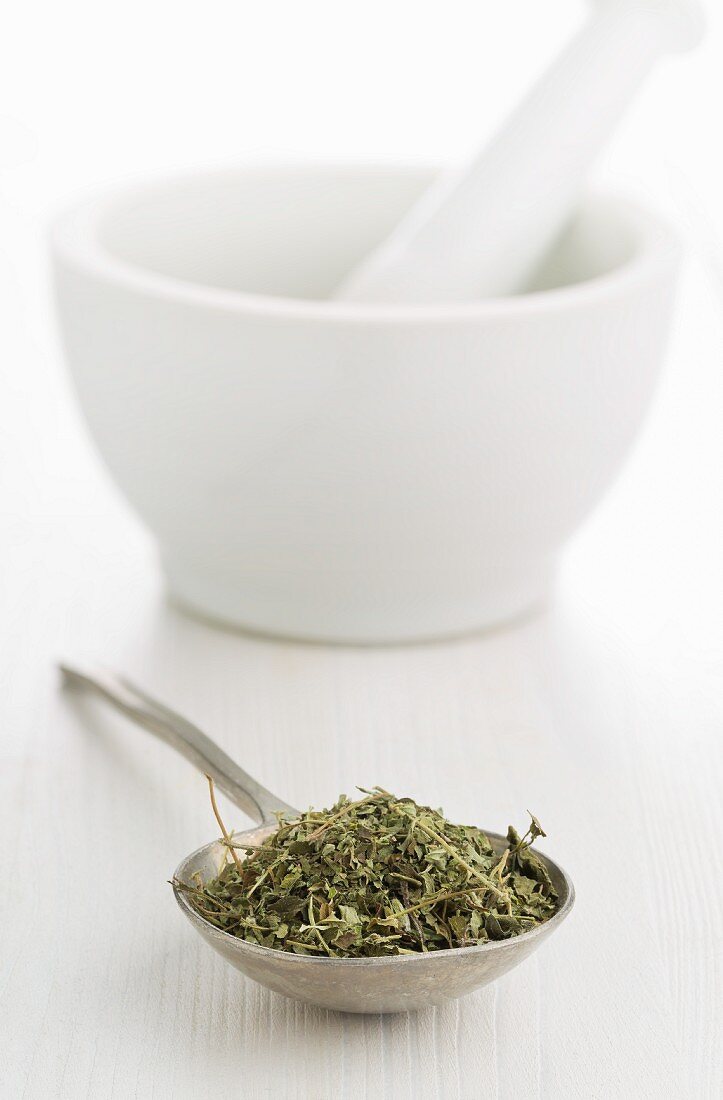 Dried oregano on a spoon in front of a mortar