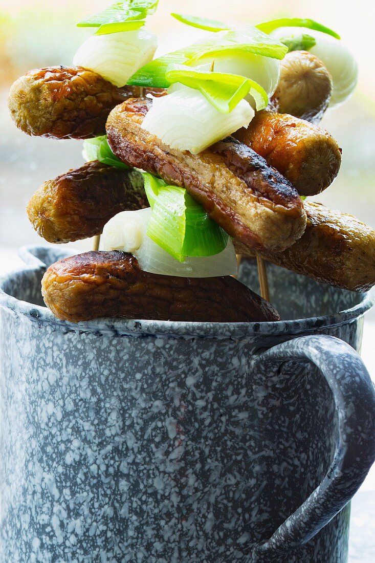 Sausages on sticks with onions and leak in an enamel mug