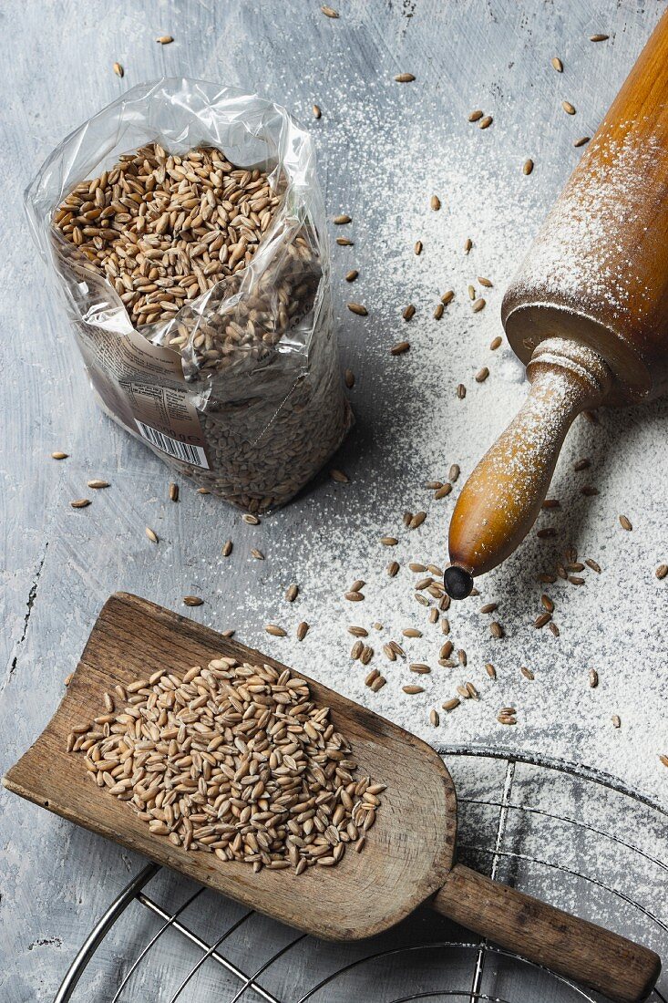 Spelt grains on a wooden scoop and in a plastic bag next to a rolling pin