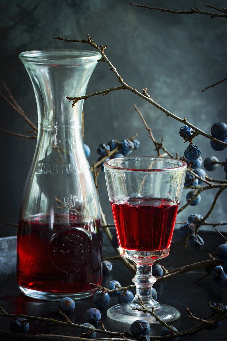 Sloe wine in a glass and a carafe with a sprig of sloes in the background