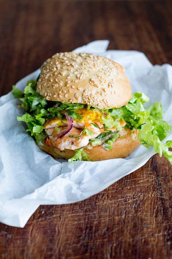 A salmon burger with green lettuce, onions and sauce