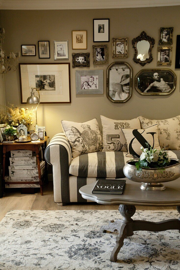 Striped couch with scatter cushions below gallery of photos on pale grey wall in vintage-style living room