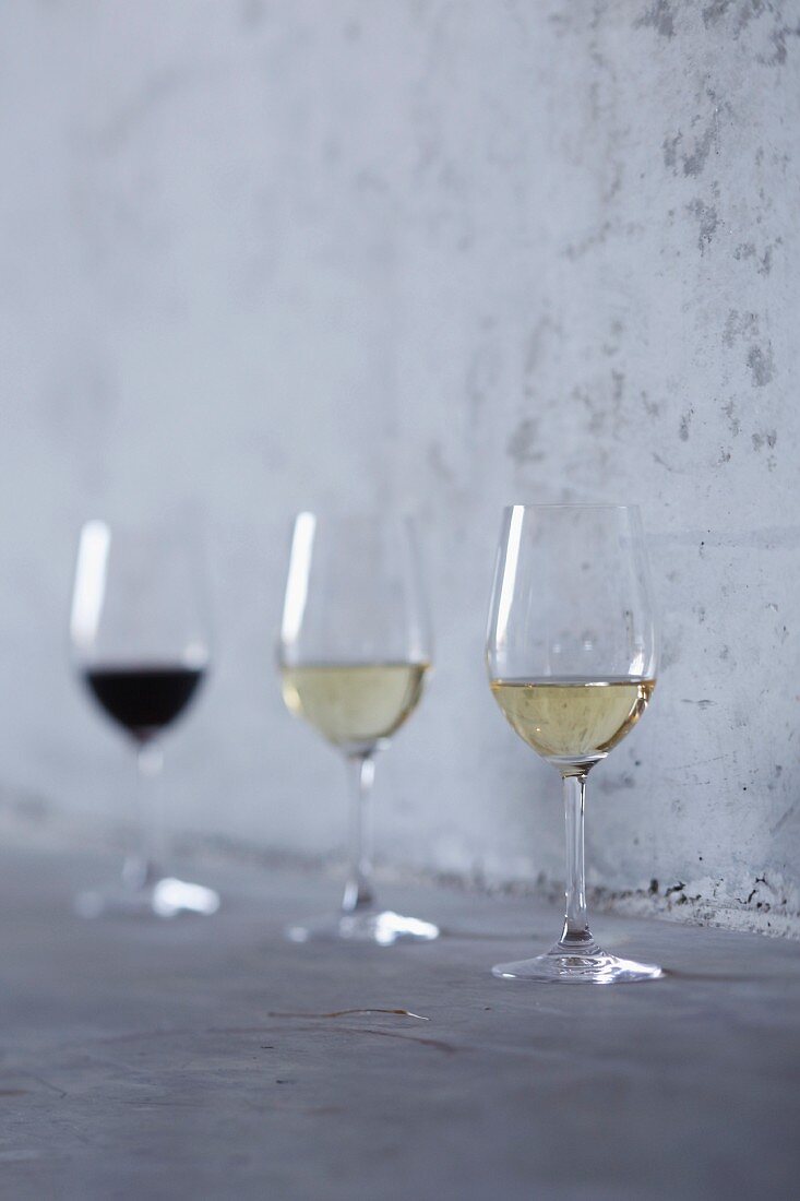 A glass of red wine and two glasses of white wine standing against a stone wall