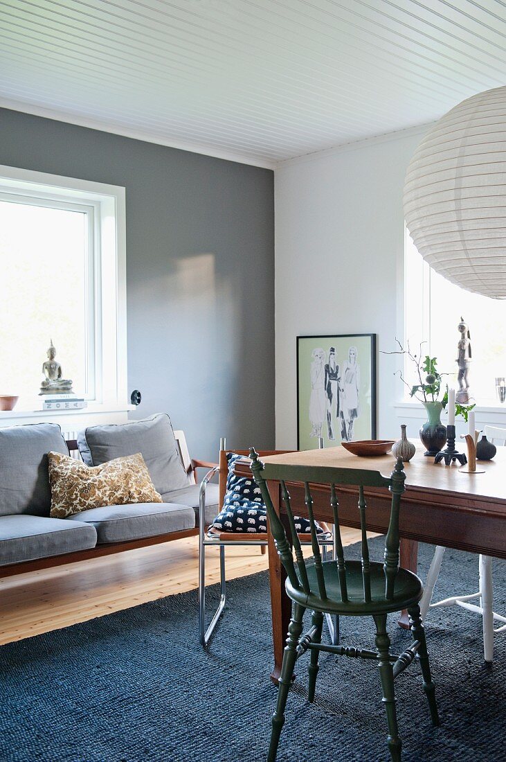 Dining table and various chairs opposite couch below window