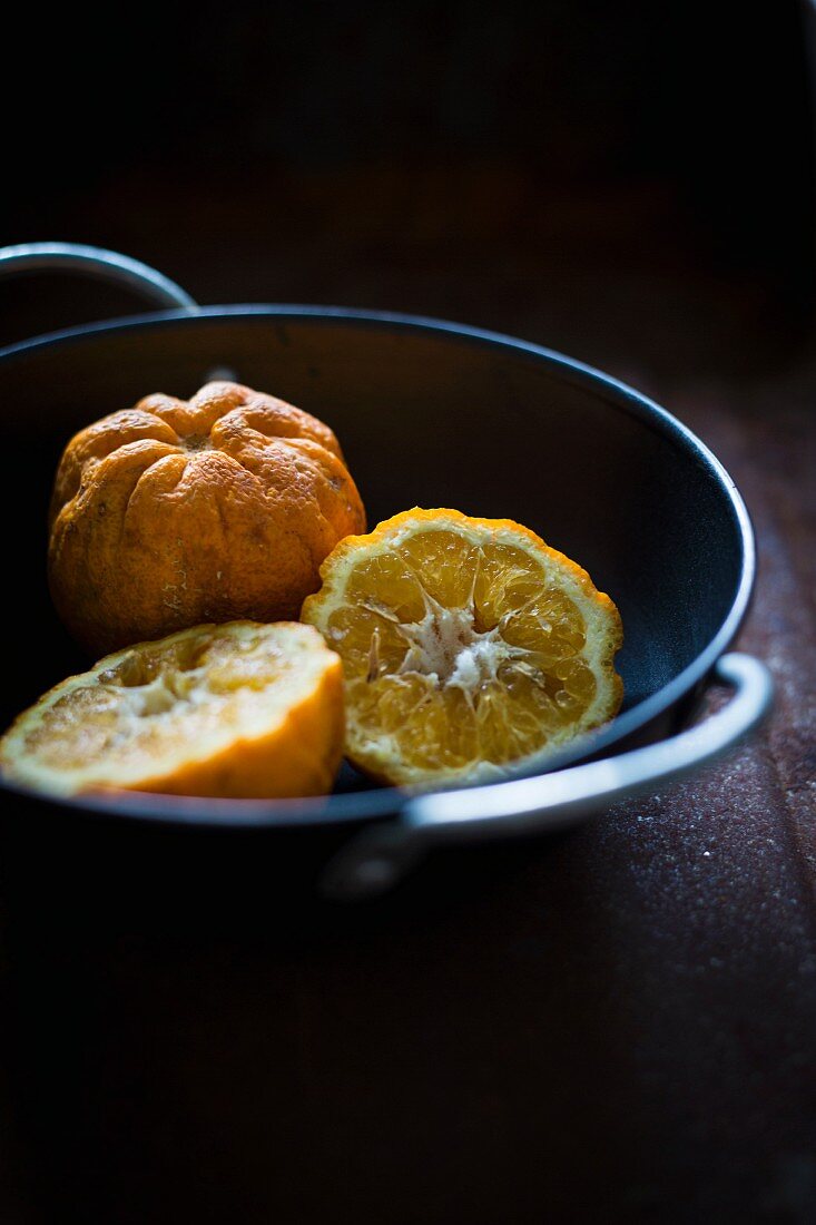 Whole and halved Seville oranges in a black bowl
