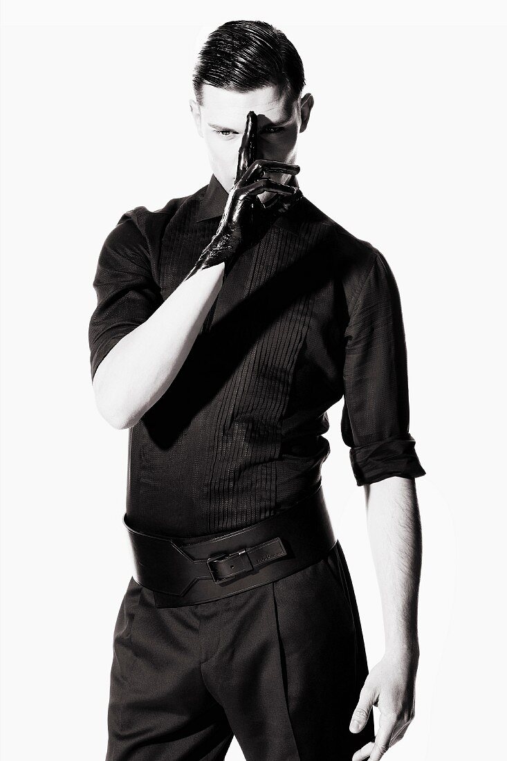 Junger Mann in schwarzer Kleidung mit einem Latexhandschuh (s/w-Foto)