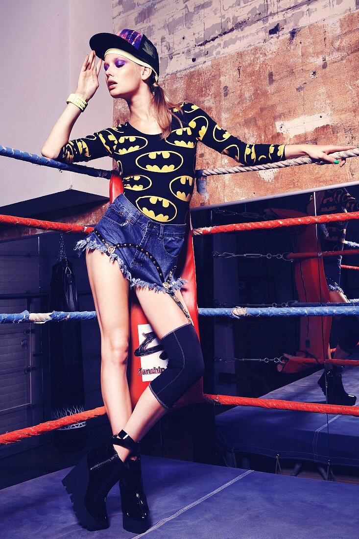 Junge Frau in Denim-Shorts und Batman-Shirt steht in Boxring
