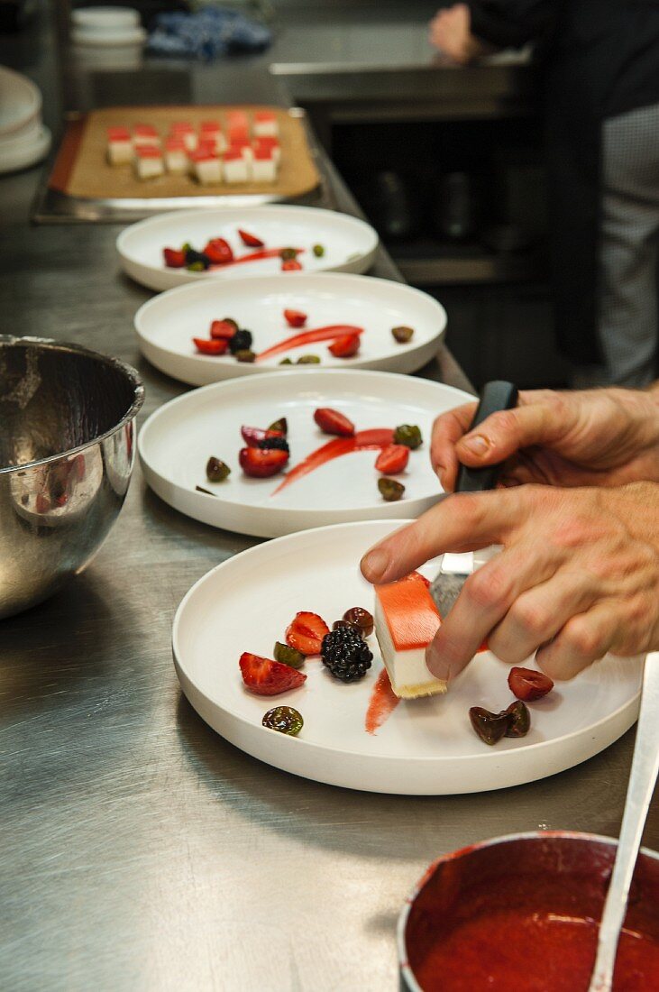 A chef in a restaurant kitchen plating up desserts