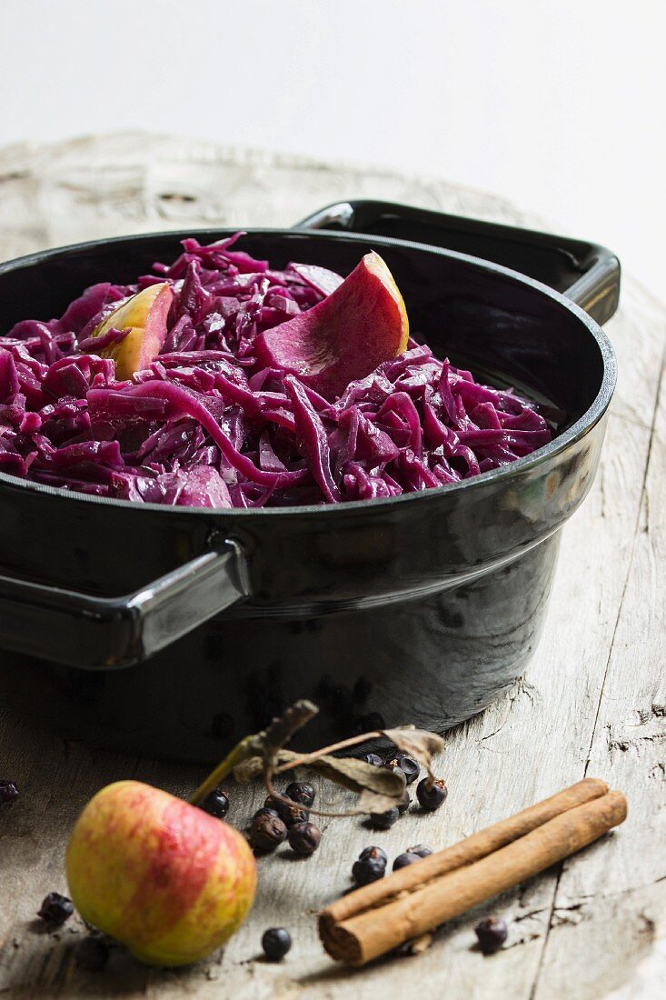 Red cabbage with apples, cinnamon and juniper berries in a back pot on a wooden board