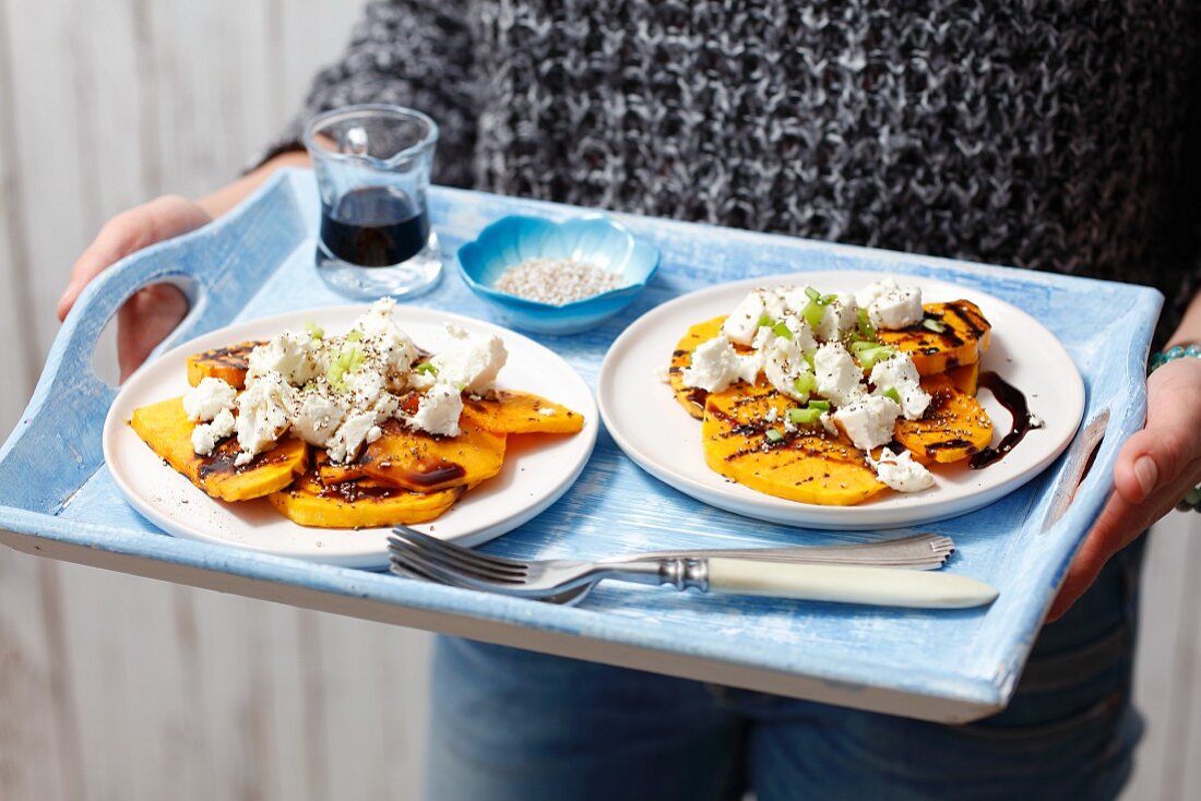 A woman holding plates of grilled pumpkin with goat's cheese on a tray