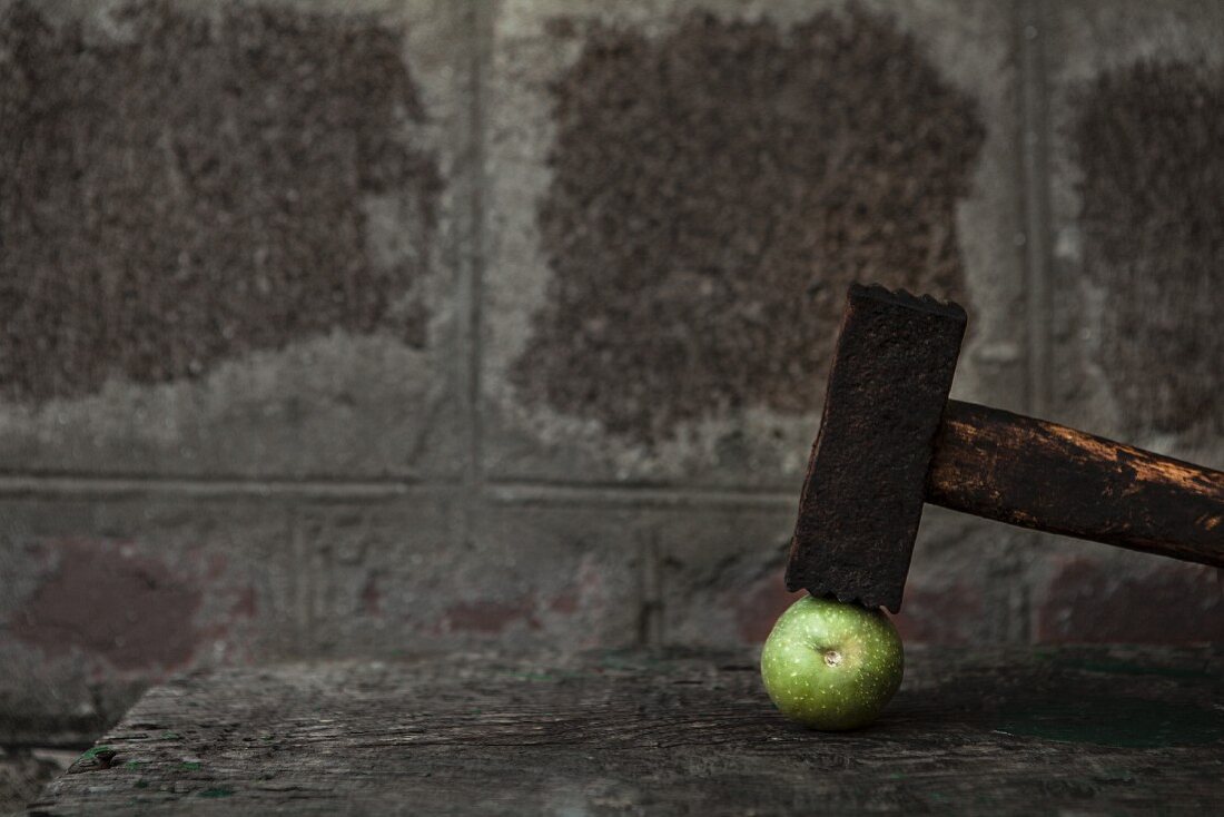 A green walnut with a hammer on a wooden table