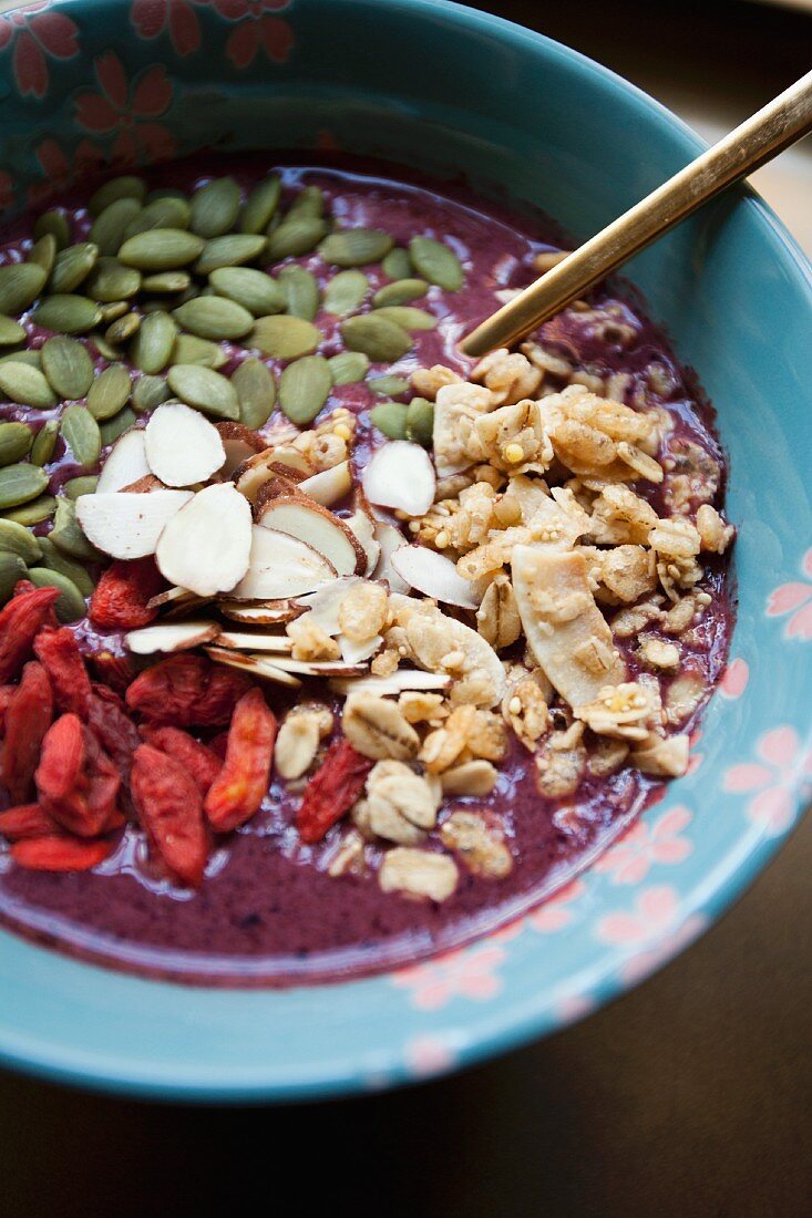 Acai smoothie in a bowl with pumpkin seeds, almonds, cereals and goji berries