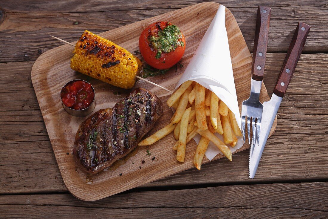 Gegrilltes Rindersteak mit Maiskolben und Pommes frites auf Holzbrett