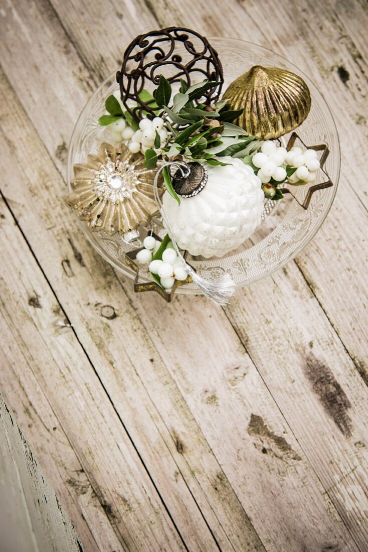 Vintage Christmas decorations and snowberries on glass cake stand on wooden table