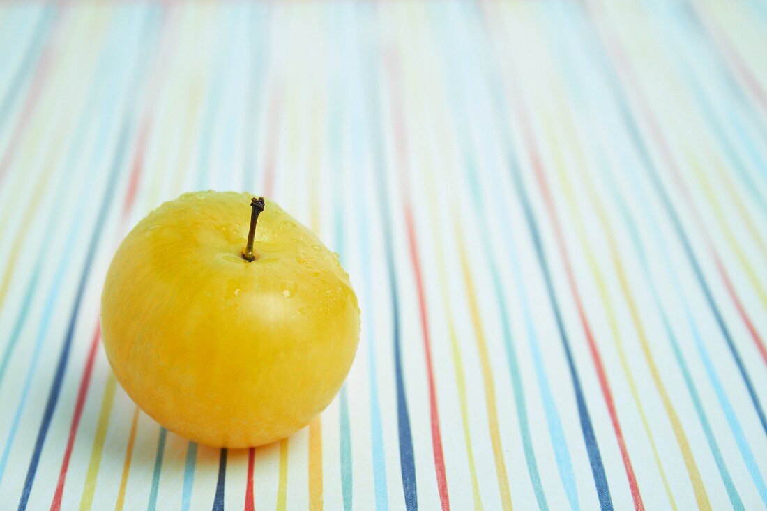 A yellow plum on a brightly coloured tablecloth