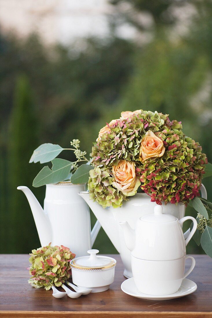 Porzellankannen und festlicher Blumenstrauss aus apricotfarbenen Rosen und Hortensien