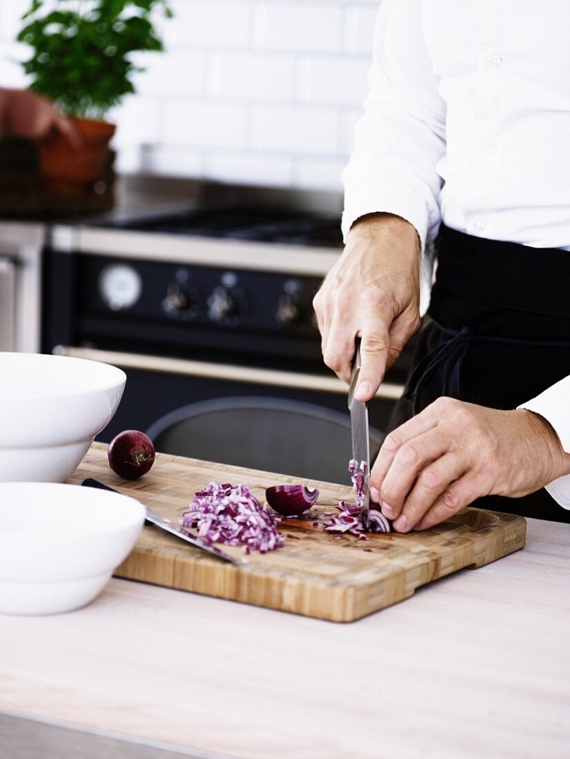 A man chopping onions on a wooden board in a kitchen