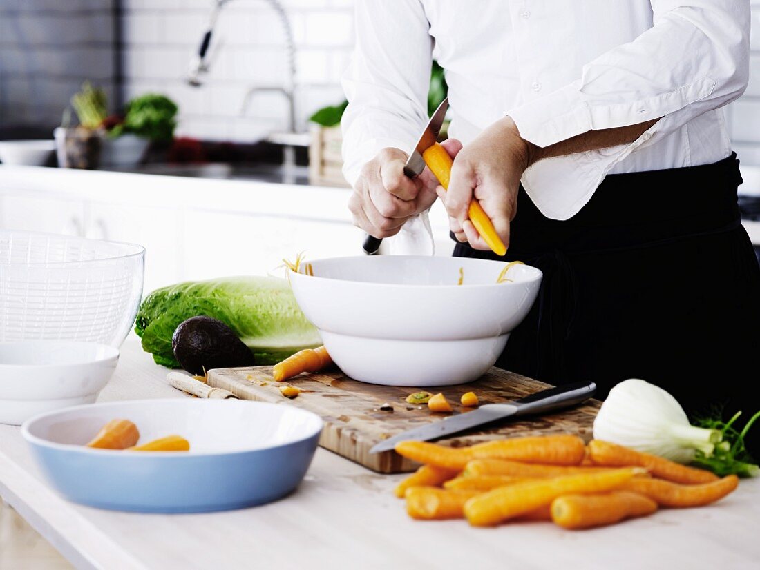 Mann schneidet putzt Karotten über Schüssel in Küche