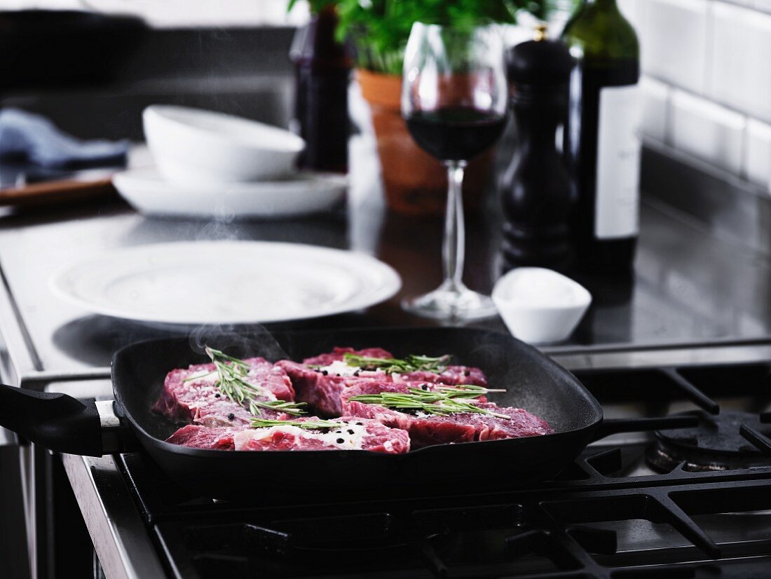 Beef steaks with rosemary being fried in a pan